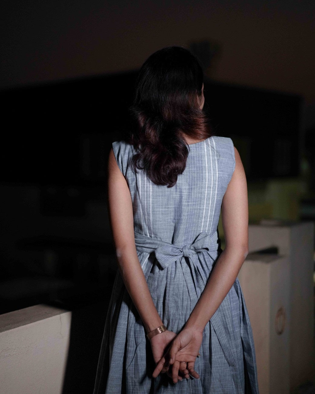 Back view of a woman in a comfortable blue dress with intricate embroidery from the Vestures collection, standing on a terrace.