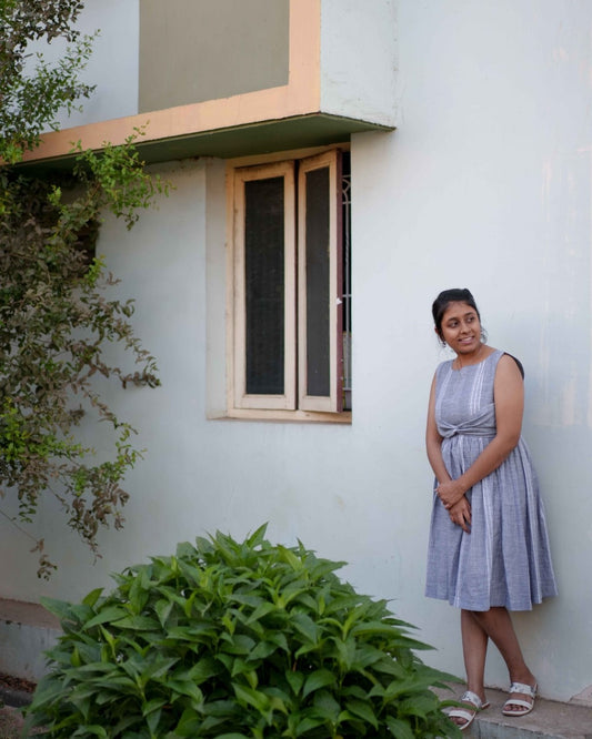A woman in a beautifully embroidered blue dress stands gracefully near a textured wall.