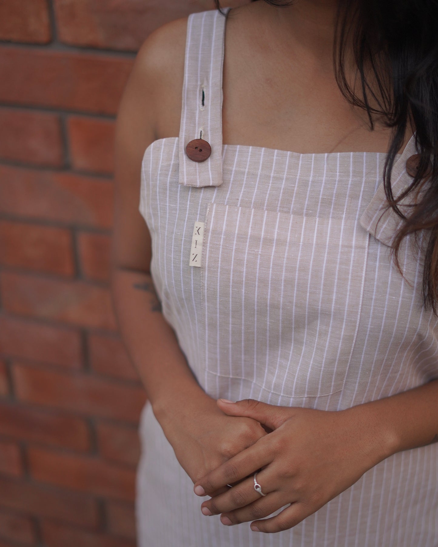 Right-side elevated close-up of a Lacey Pearl Linen Cotton Pinafore, showcasing the embedded brand label as a signature design detail.