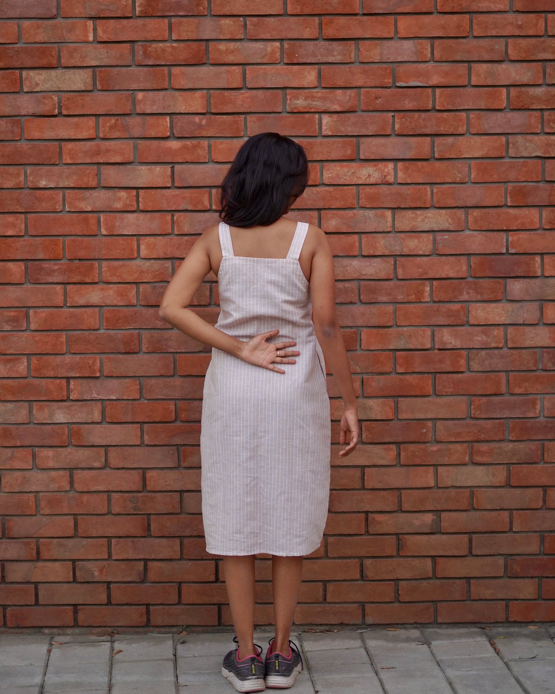 Full back view of a woman in a Lacey Pearl Linen Cotton Pinafore, showcasing the dress’s comfortable fit and elegant one-piece design.