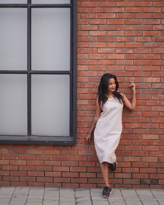 A woman leans on a brown brick wall wearing a Lacey Pearl Color Cozy One-Piece Pinafore, with a vibrant mirror contrast highlighting the dress’s elegance.