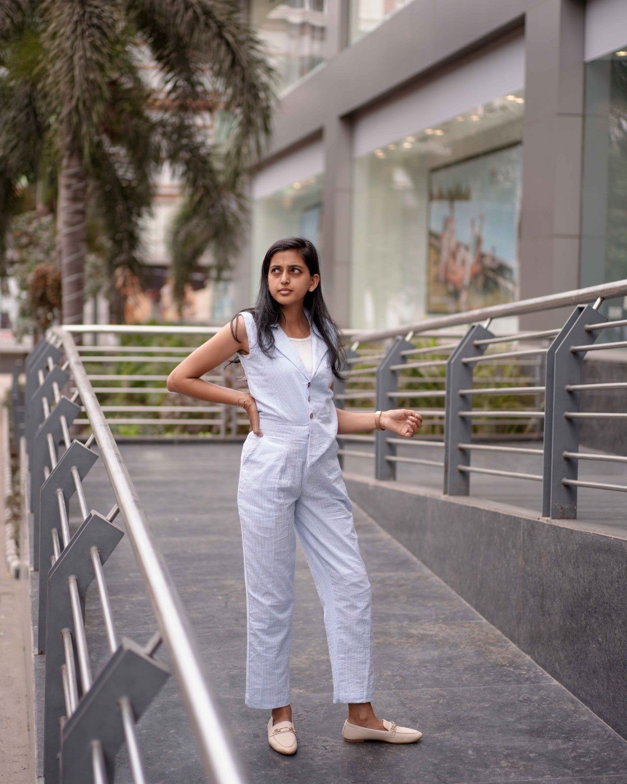 A woman in the Anki Jumpsuit elegantly poses on a lawn pathway, exuding confidence and effortless style.