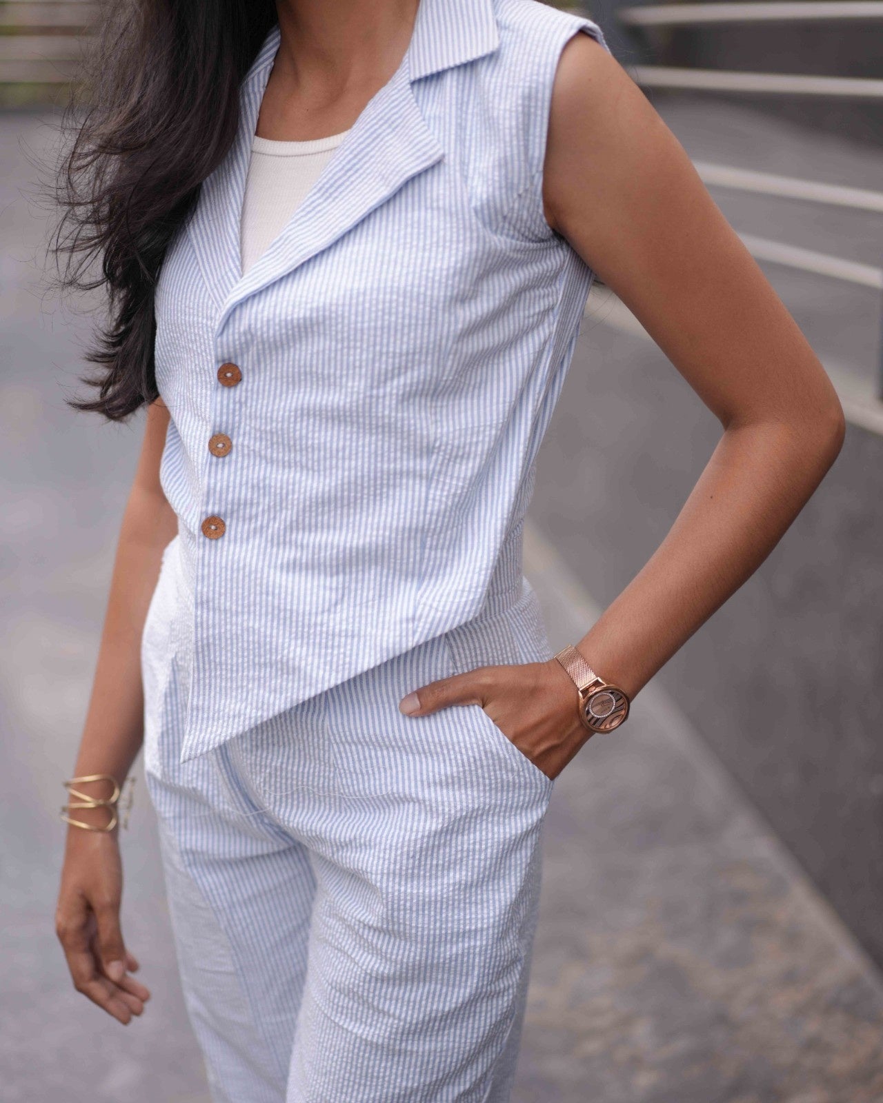 Close-up of a woman wearing the Anki Jumpsuit in White and Breeze Blue, styled with a contrast rose gold watch and hands tucked into pockets.