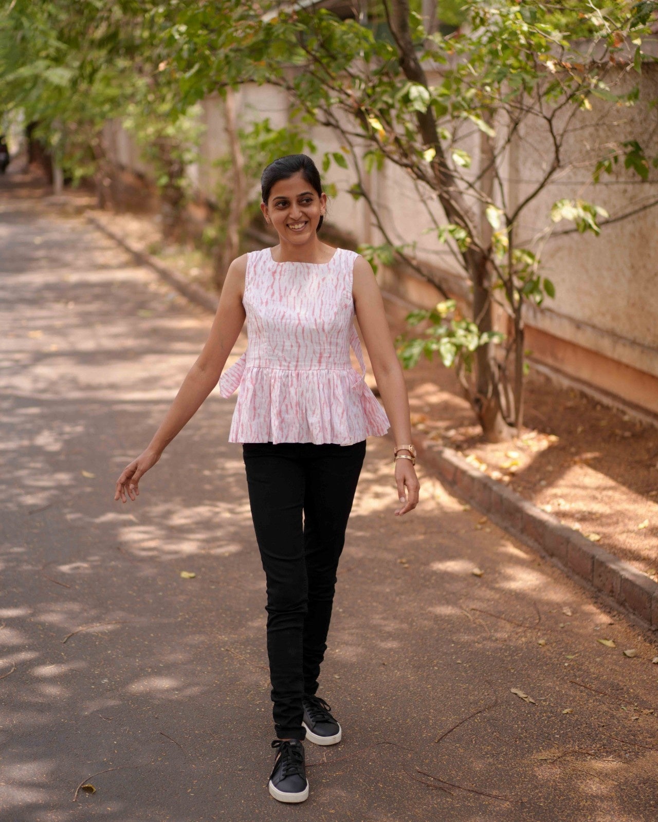A woman elegantly walks on a brown sand road, making the Pink & White Vil Top stand out with a bold and stylish contrast.