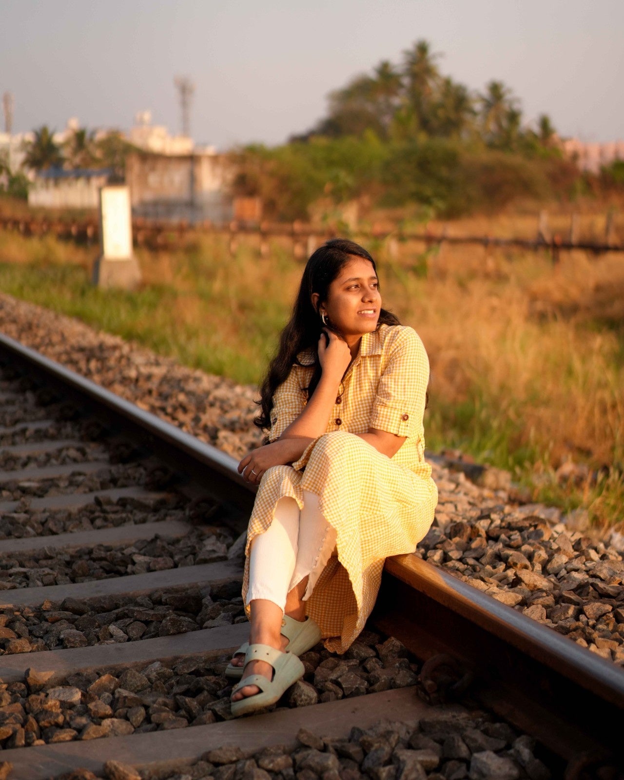 A woman sitting gracefully on a railway track, feeling confident and carefree in a Yellow and White checked linen shirt dress.